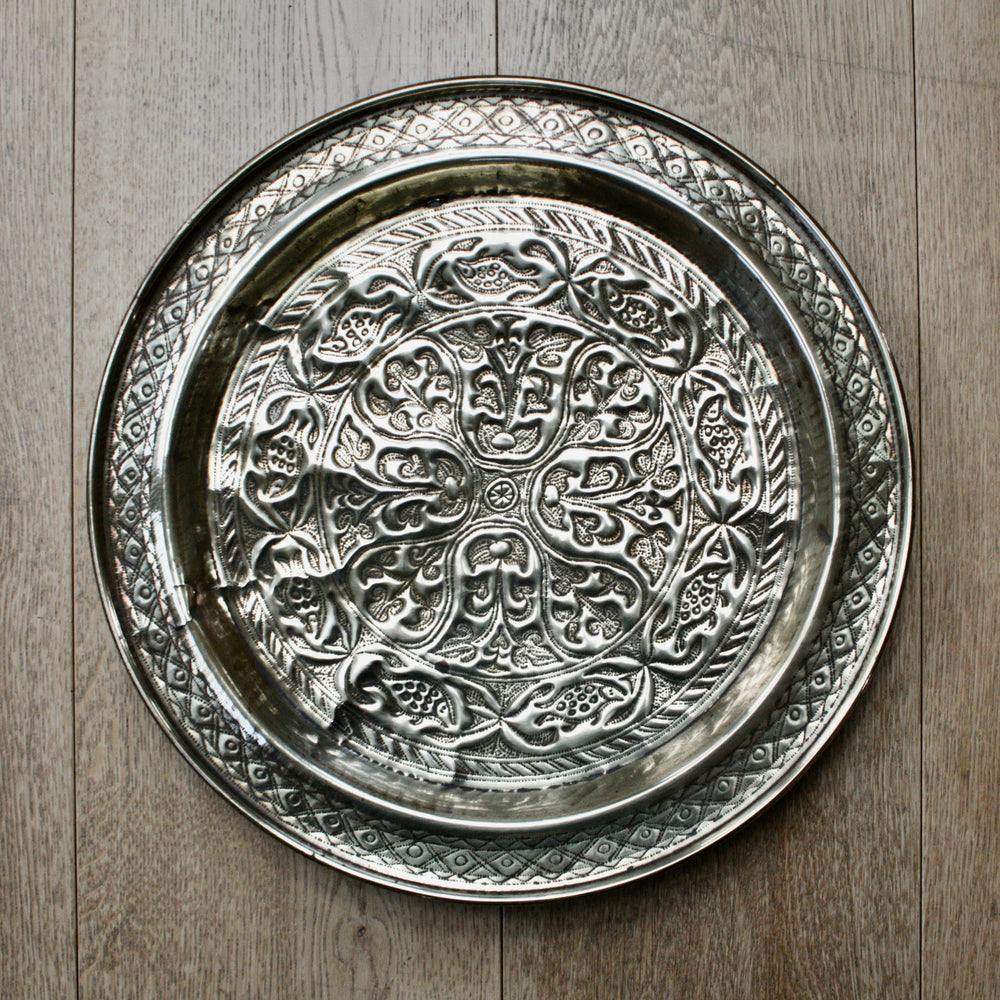 an antique african efic brass charger embossed with wild plants and fish.